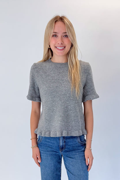 Front view of woman wearing Swagger Boutique’s Grey Ruffle Hem Sweater with jeans against white studio background.