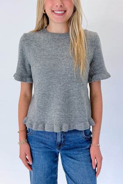 Front detail view of woman wearing Swagger Boutique’s Grey Ruffle Hem Sweater with jeans against white studio background.