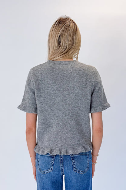 Back view of woman wearing Swagger Boutique’s Grey Ruffle Hem Sweater with jeans against white studio background.