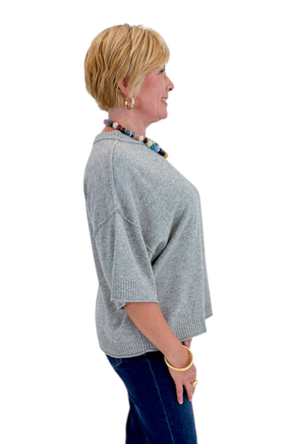 Side view of woman wearing Swagger Boutique’s Grey Short Sleeve Sweater with jeans against white studio background.