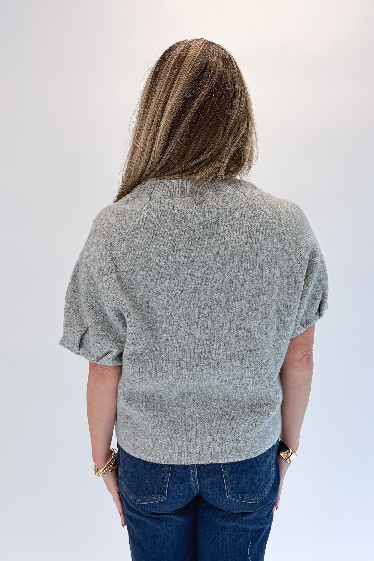 Back view of woman wearing Swagger Boutique’s Grey Short Sleeve Sweater with jeans against white studio background.