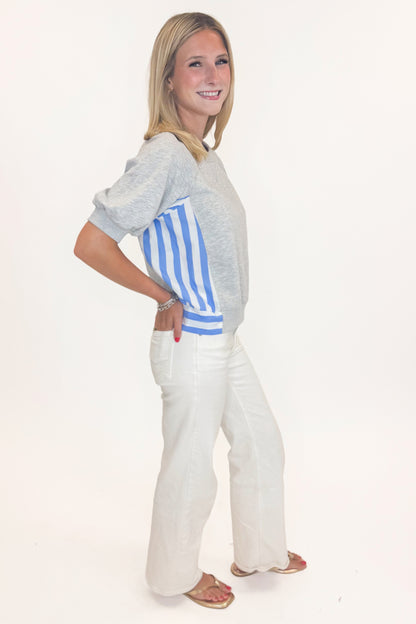 Side view of woman wearing Swagger Boutique’s Grey Striped Short Sleeve Sweatshirt with jeans against white studio background.