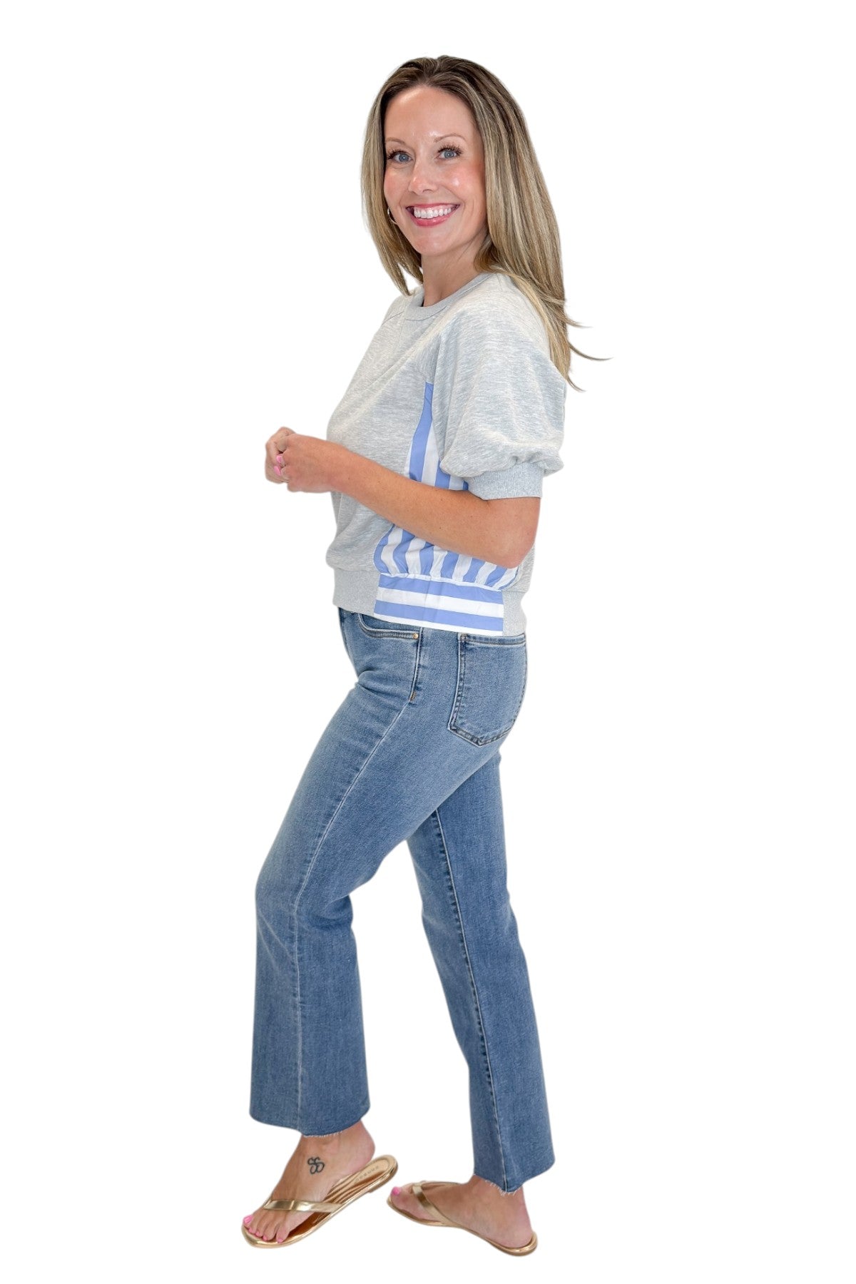 Side view of woman wearing Swagger Boutique’s Grey Striped Short Sleeve Sweatshirt with jeans against white studio background.