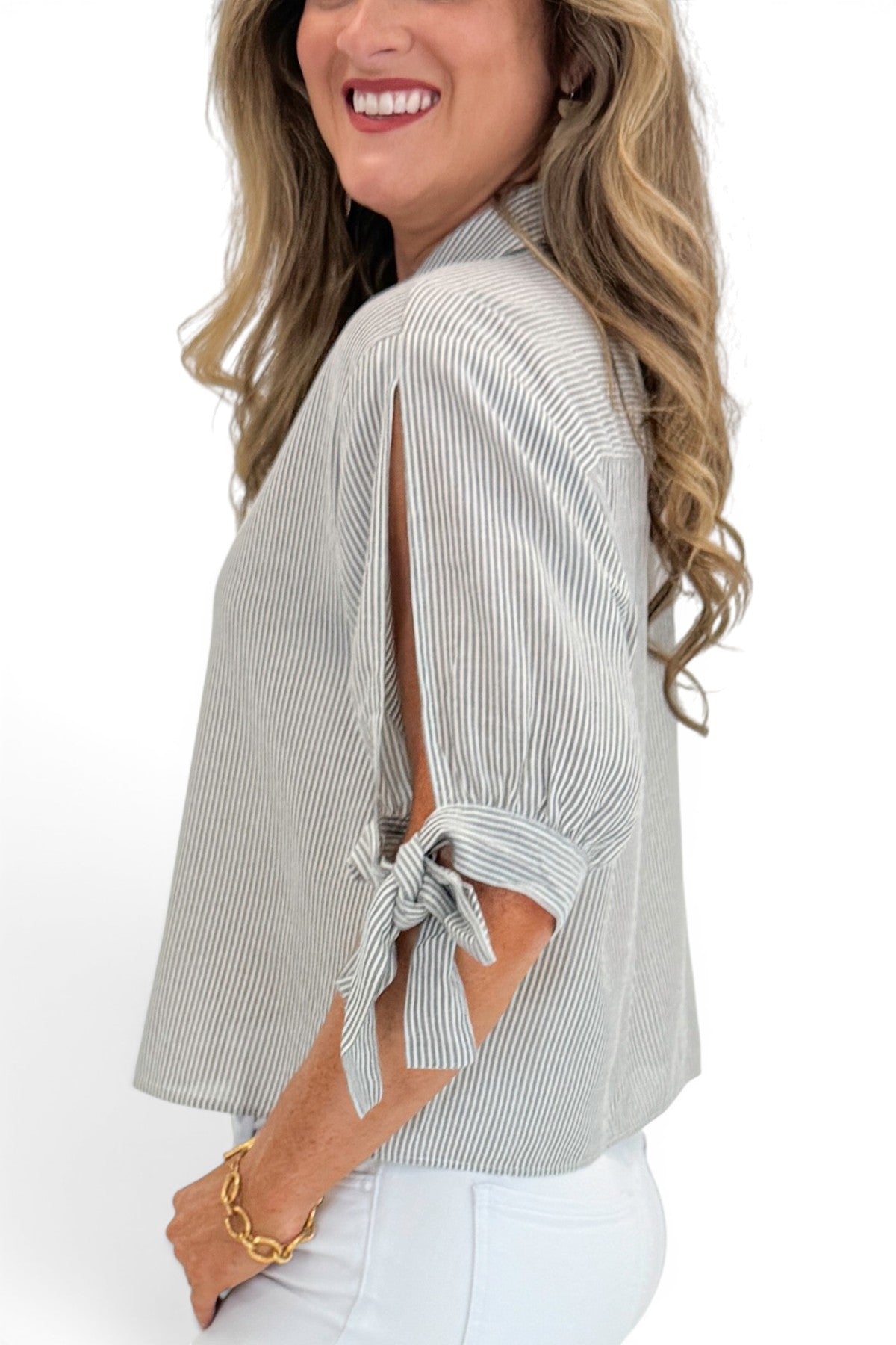 Side detail view of woman wearing Swagger Boutique’s Grey Striped Tie Sleeve Top with jeans against white studio background.