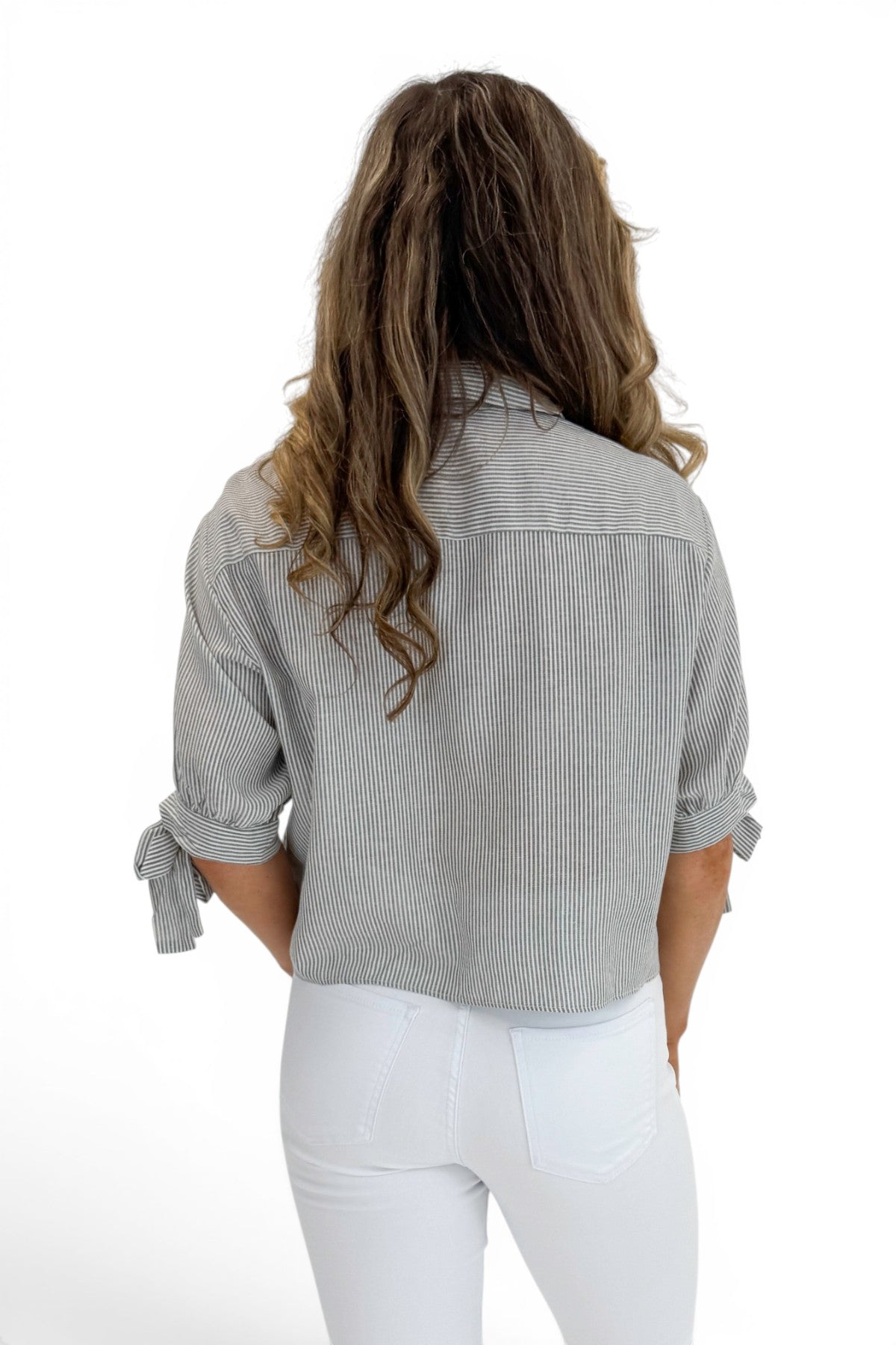 Back view of woman wearing Swagger Boutique’s Grey Striped Tie Sleeve Top with jeans against white studio background.