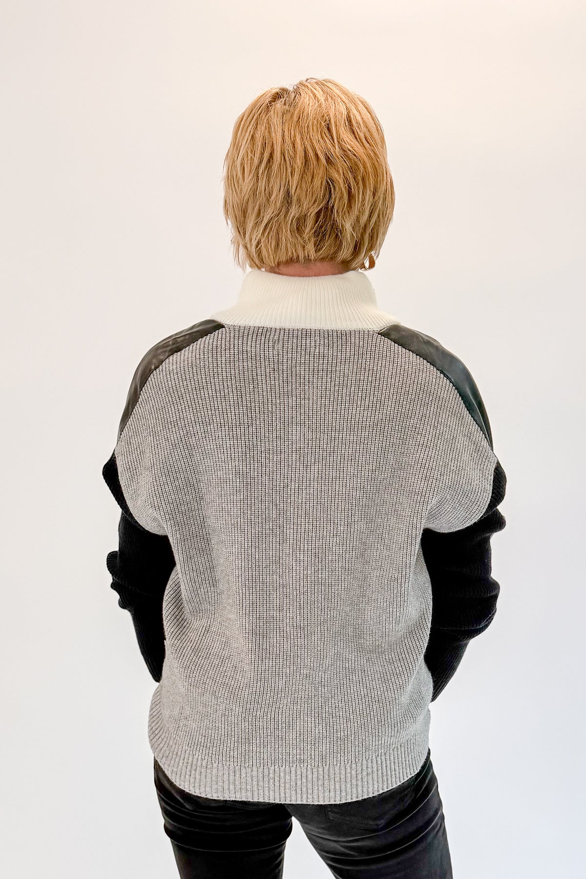 Back view of woman wearing Swagger Boutique’s Grey &amp; Black Color Block 1/4 Zip Sweater with jeans against white studio background.