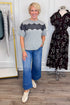 Front view of woman wearing Swagger Boutique’s Grey & Black Lace Contrast Tee with jeans with clothing hanging in the background.