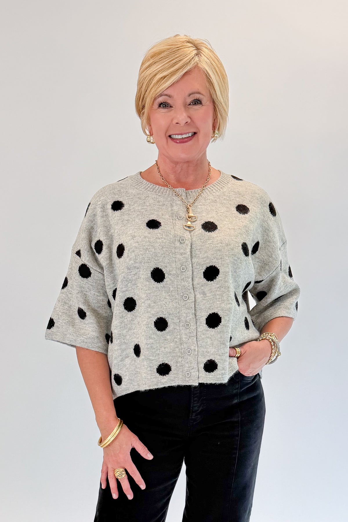 Front view of woman wearing Swagger Boutique’s Grey &amp; Black Polka Dot Short Sleeve Cardigan with jeans against white studio background.