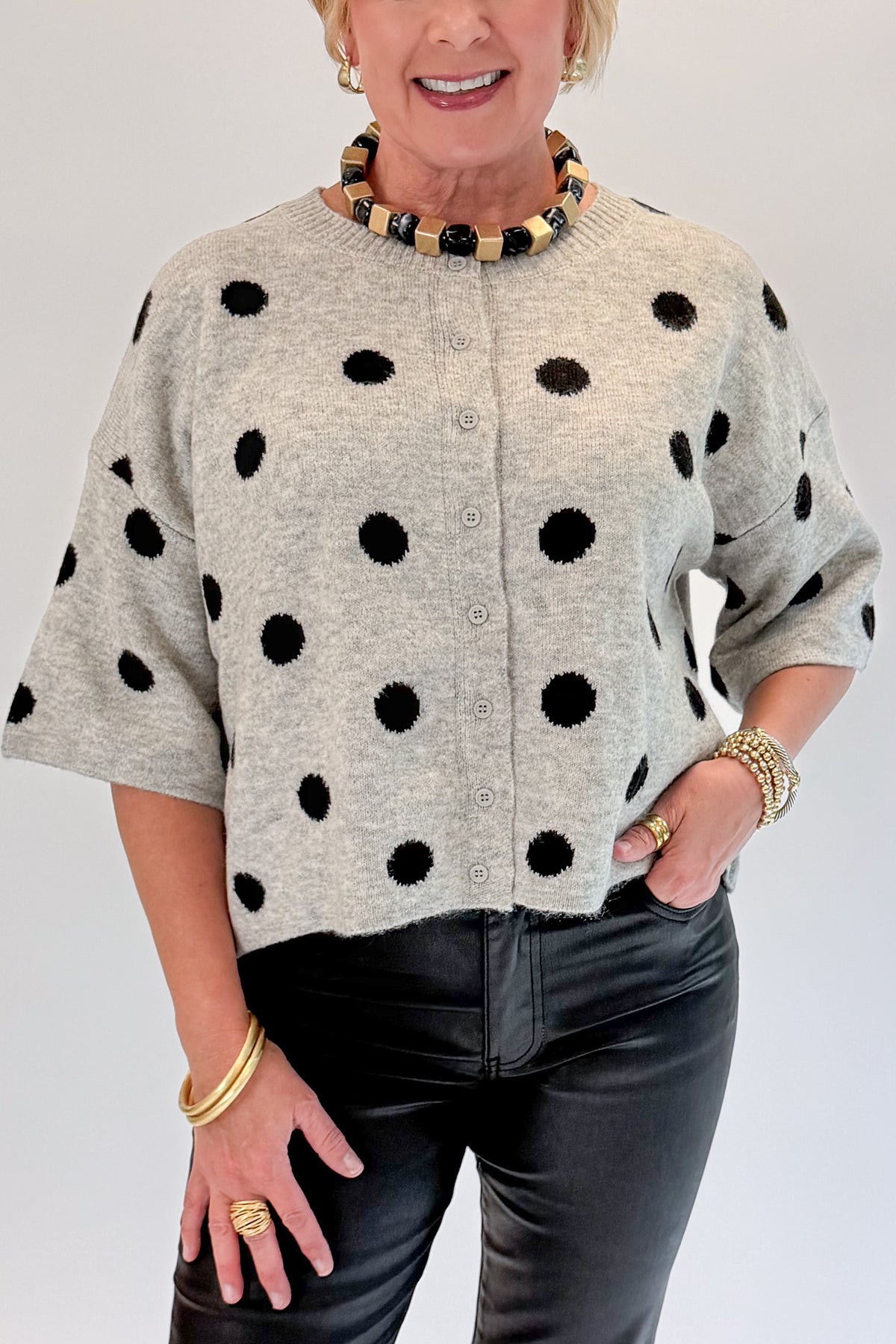 Front detail view of woman wearing Swagger Boutique’s Grey &amp; Black Polka Dot Short Sleeve Cardigan with jeans against white studio background.