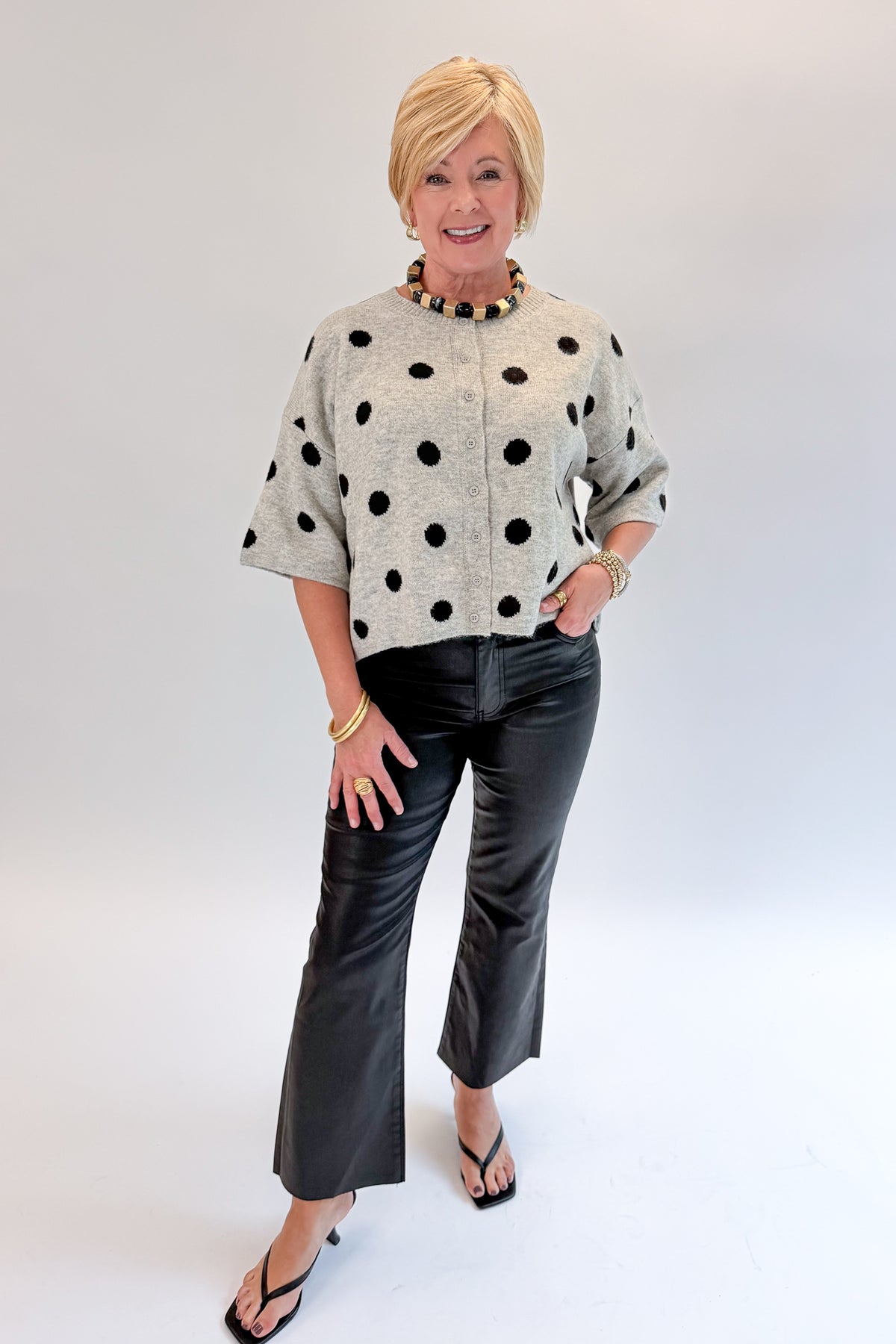 Front view of woman wearing Swagger Boutique’s Grey &amp; Black Polka Dot Short Sleeve Cardigan with jeans against white studio background.