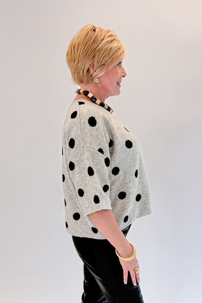 Side view of woman wearing Swagger Boutique’s Grey &amp; Black Polka Dot Short Sleeve Cardigan with jeans against white studio background.