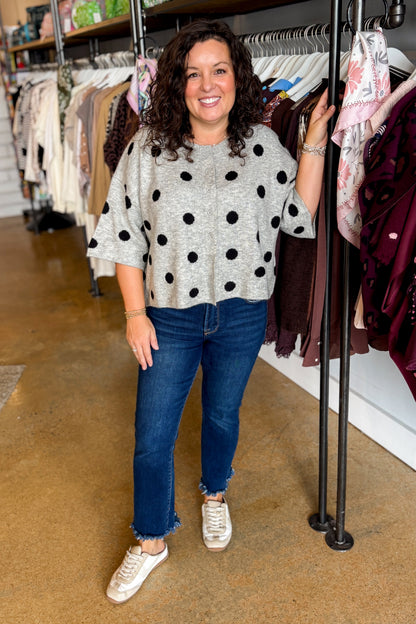 Front view of woman wearing Swagger Boutique’s Grey &amp; Black Polka Dot Short Sleeve Cardigan with jeans standing at the store.