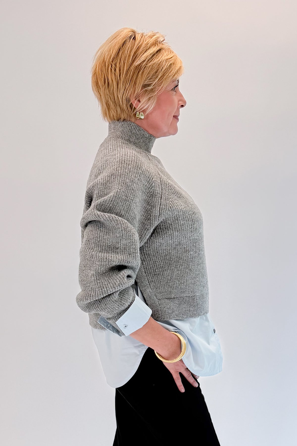 Side view of woman wearing Swagger Boutique’s Grey &amp; Blue Layered Sweater &amp; Shirt by Entro with jeans against white studio background.