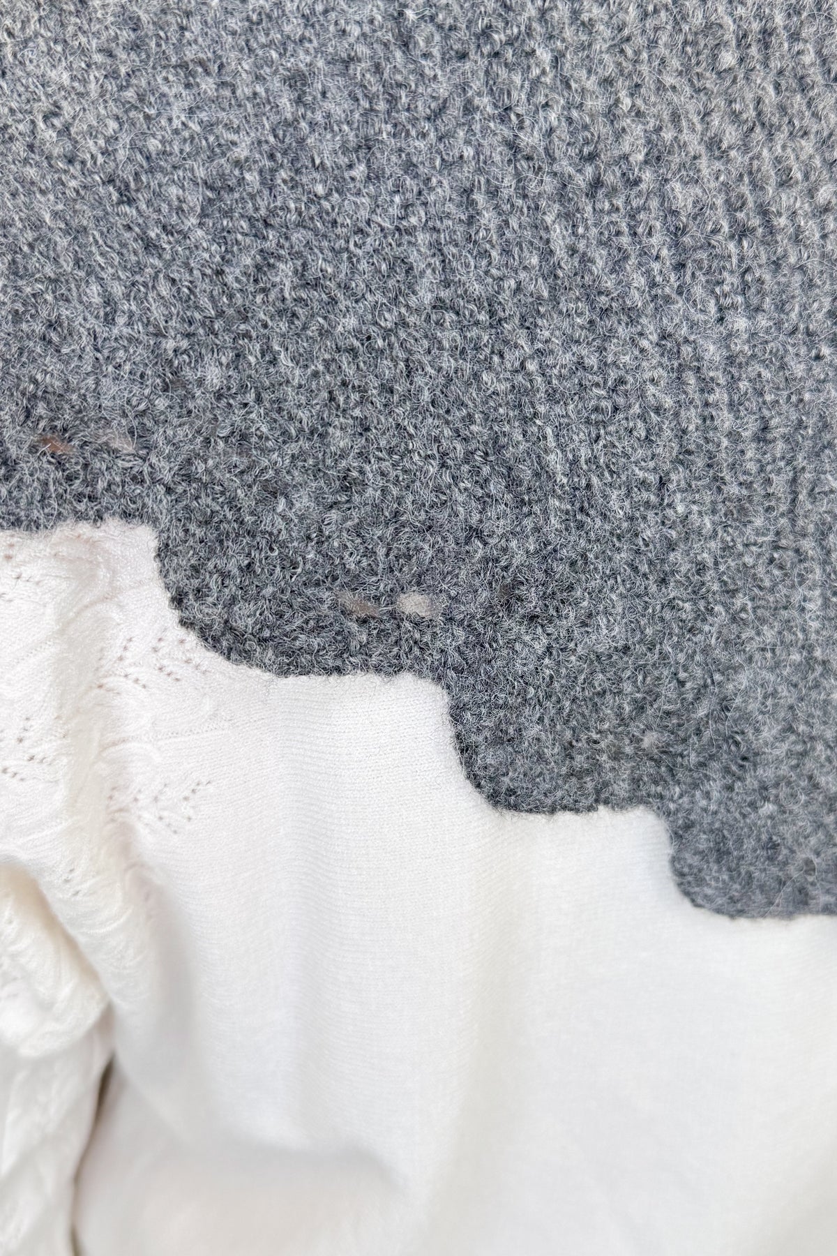 Close-up of a gray knit fabric with a scalloped edge over a white textured fabric.