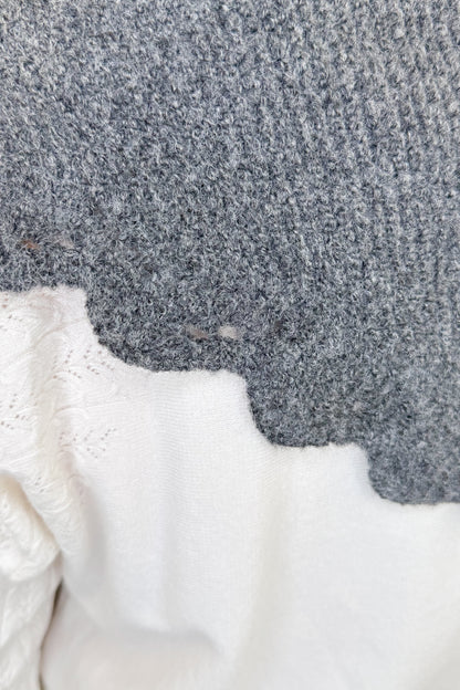 Close-up of a gray knit fabric with a scalloped edge over a white textured fabric.