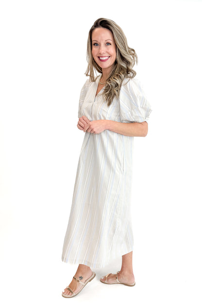 Side view of woman wearing Beige &amp; Light Blue Striped Midi Dress against white studio background.