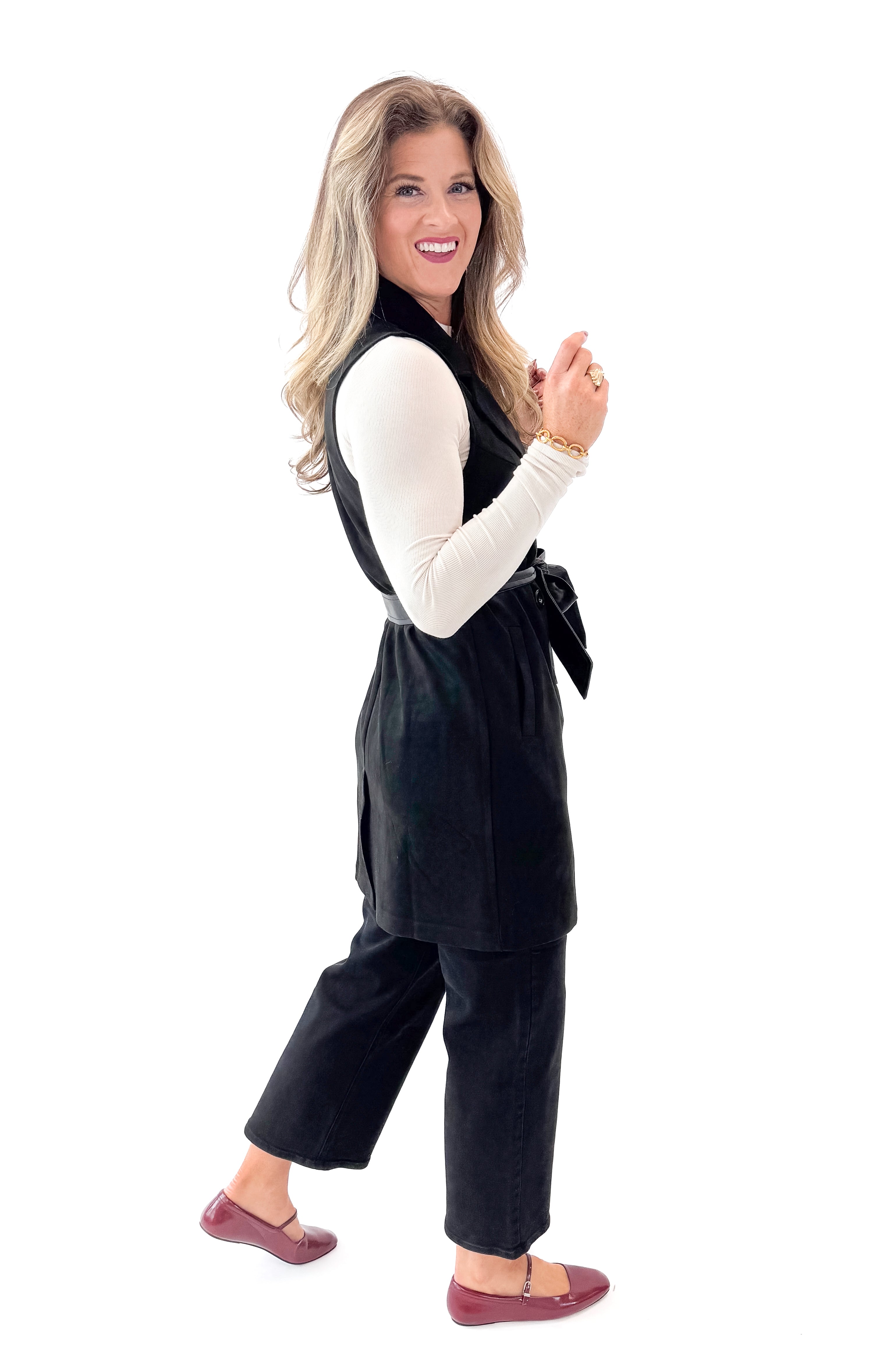 Side view of woman wearing Black Suede Long Vest with jeans against white studio background.
