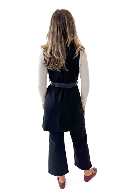 Back view of woman wearing Black Suede Long Vest with jeans against white studio background.