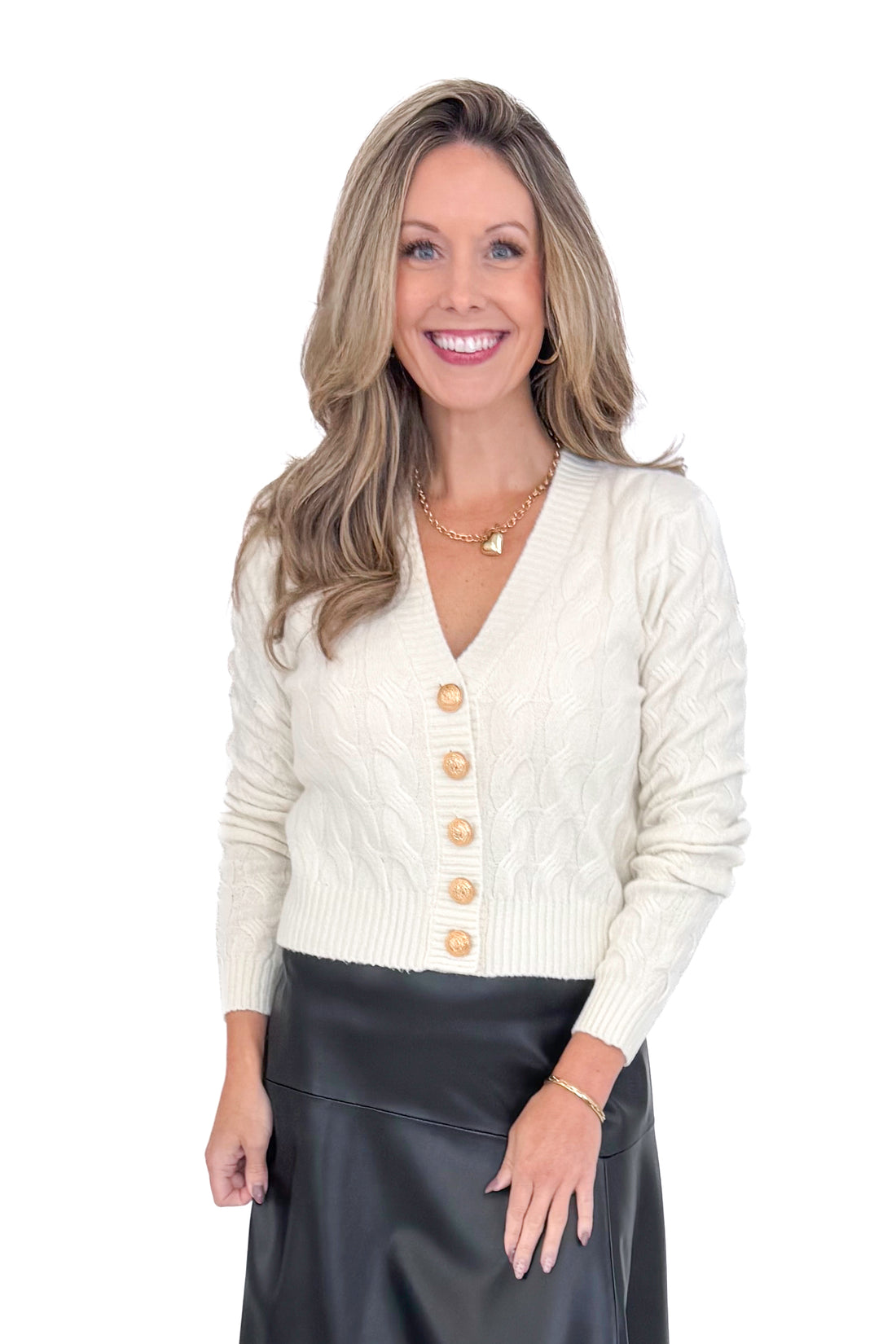 Front view of woman wearing Cream Cable Knit Button Up Cardigan with black skirt against white studio background.