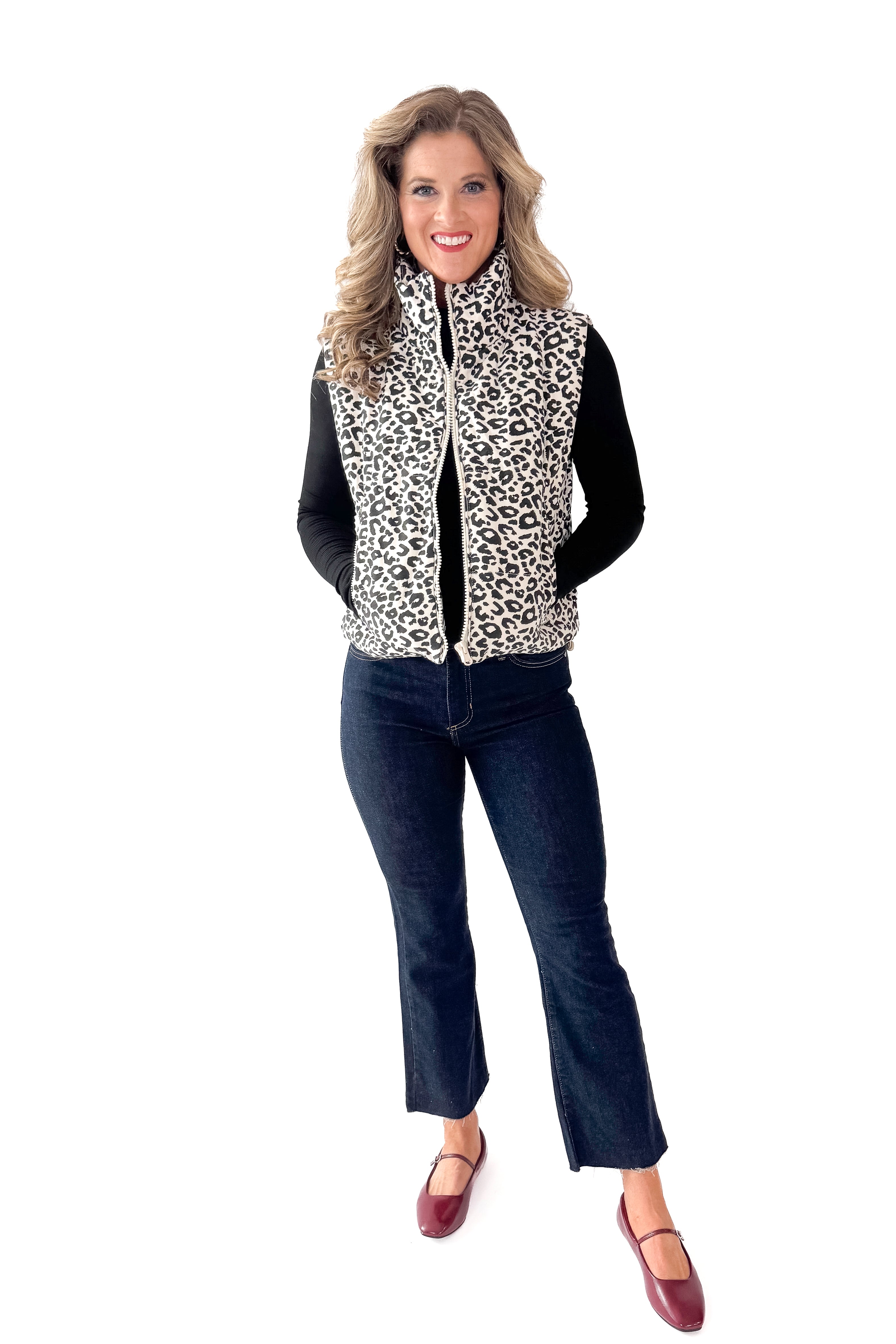 Front view of woman wearing Cream Leopard Puffer Vest with jeans against white studio background.