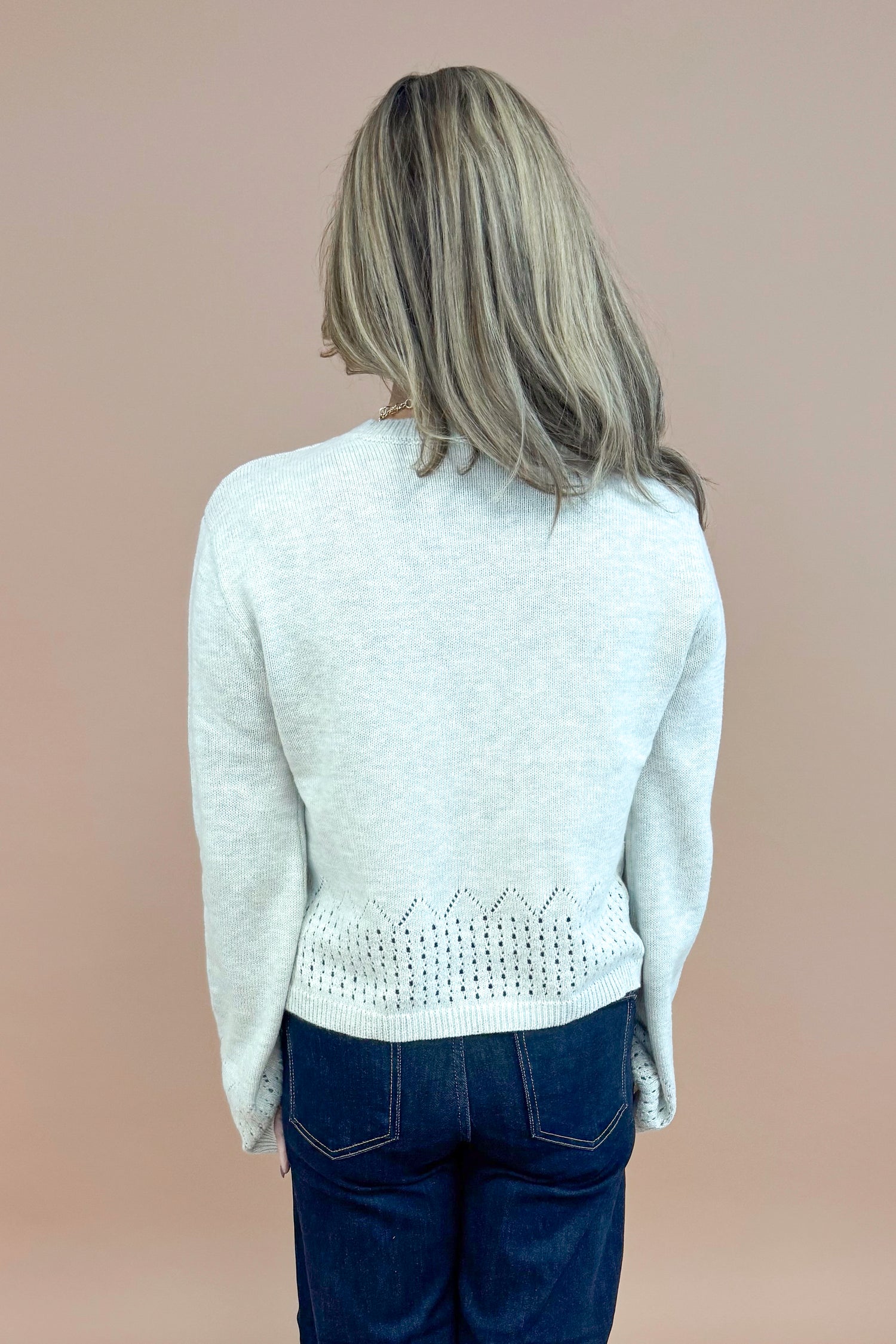 Back view of woman wearing Grey Cutout Detail Sweater and blue jeans. 