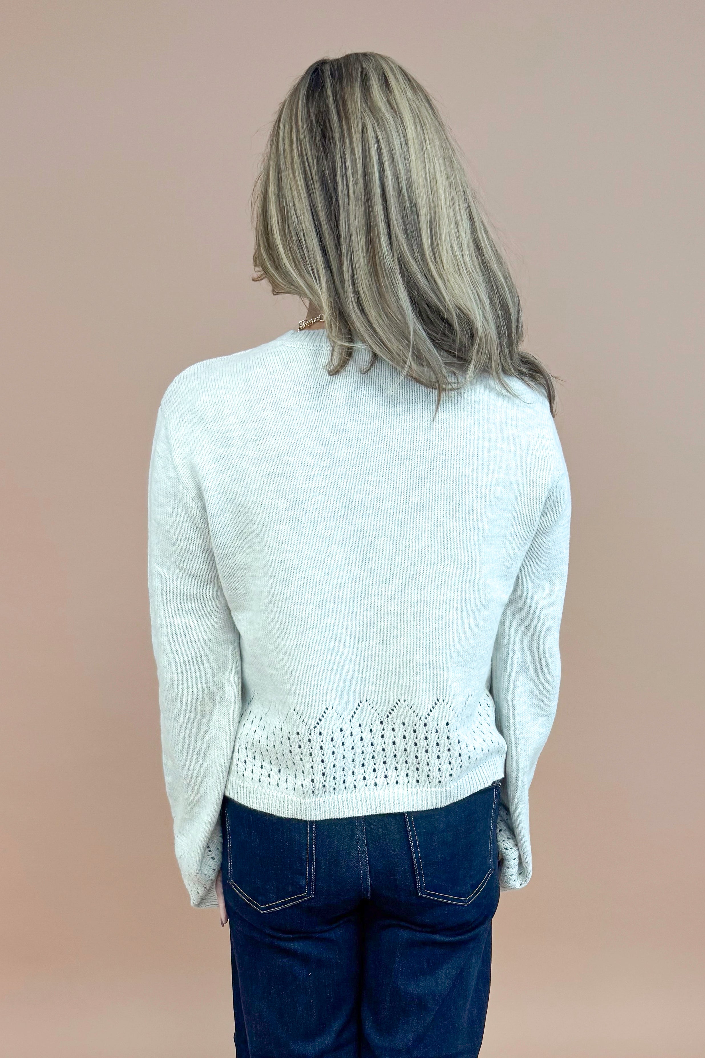 Back view of woman wearing Grey Cutout Detail Sweater and blue jeans. 