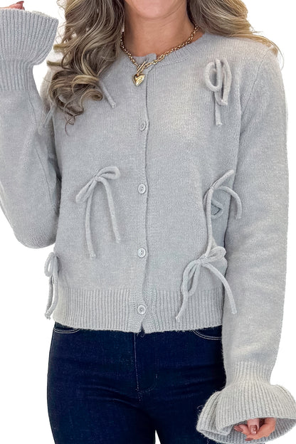 Front detail view of woman wearing Grey Button Up Bow Detail Sweater with jeans against white studio background.