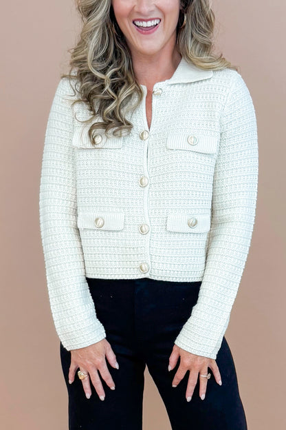 Detailed view of woman wearing Cream Textured Button Up Cardigan with taupe background.
