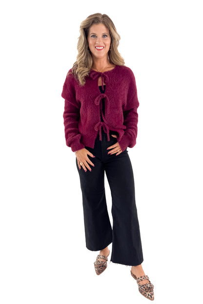 Front view of woman wearing Wine Eyelash Tie Detail Cardigan with jeans against white studio background.