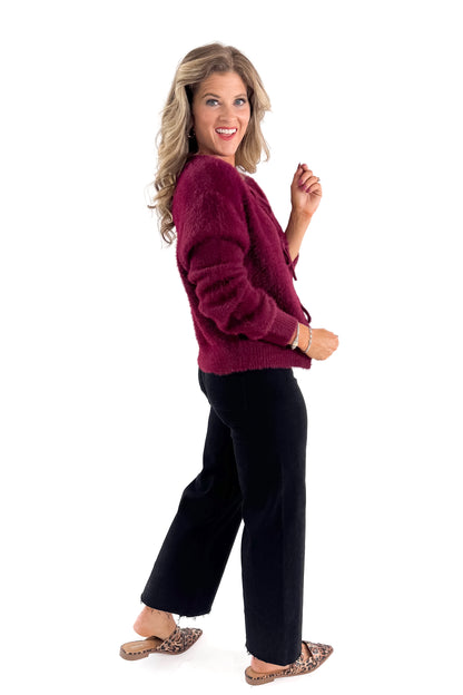 Side view of woman wearing Wine Eyelash Tie Detail Cardigan with jeans against white studio background.