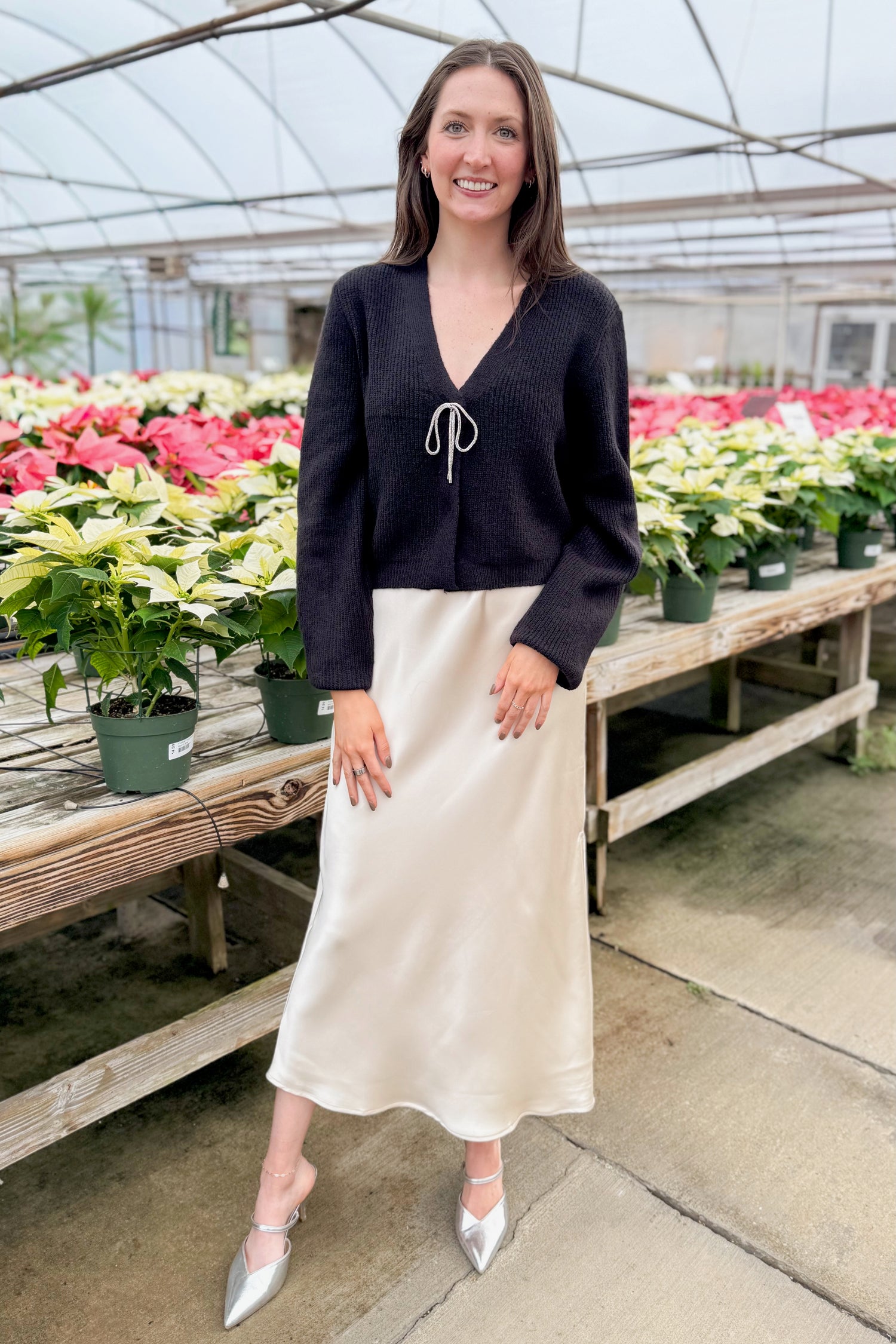 Front view of woman wearing Black Cardigan With Rhinestone Bow with skirt  with holiday decor background.