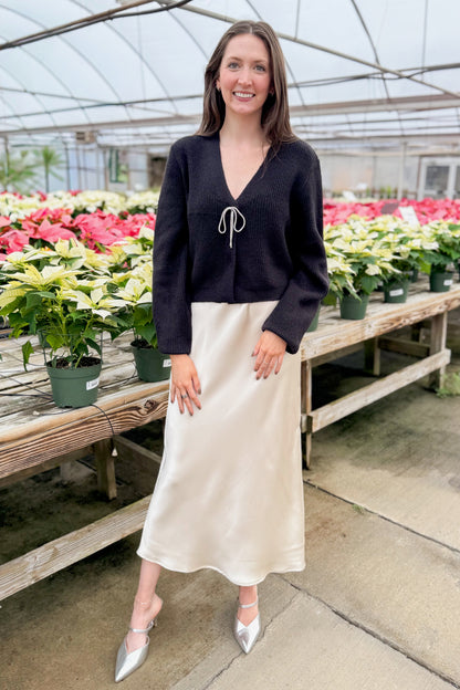 Front view of woman wearing Black Cardigan With Rhinestone Bow with skirt  with holiday decor background.