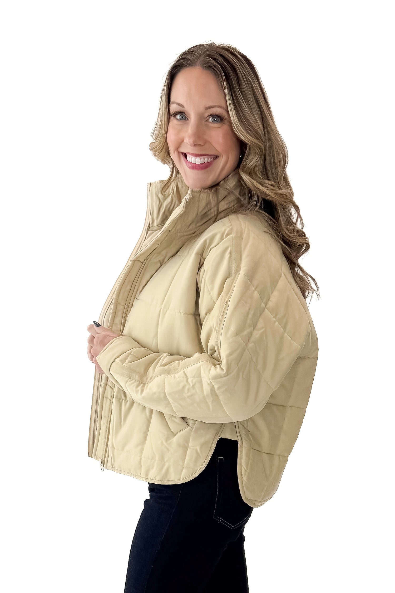 Side view of woman wearing Beige Quilted Puffer Jacket with jeans against white studio background.