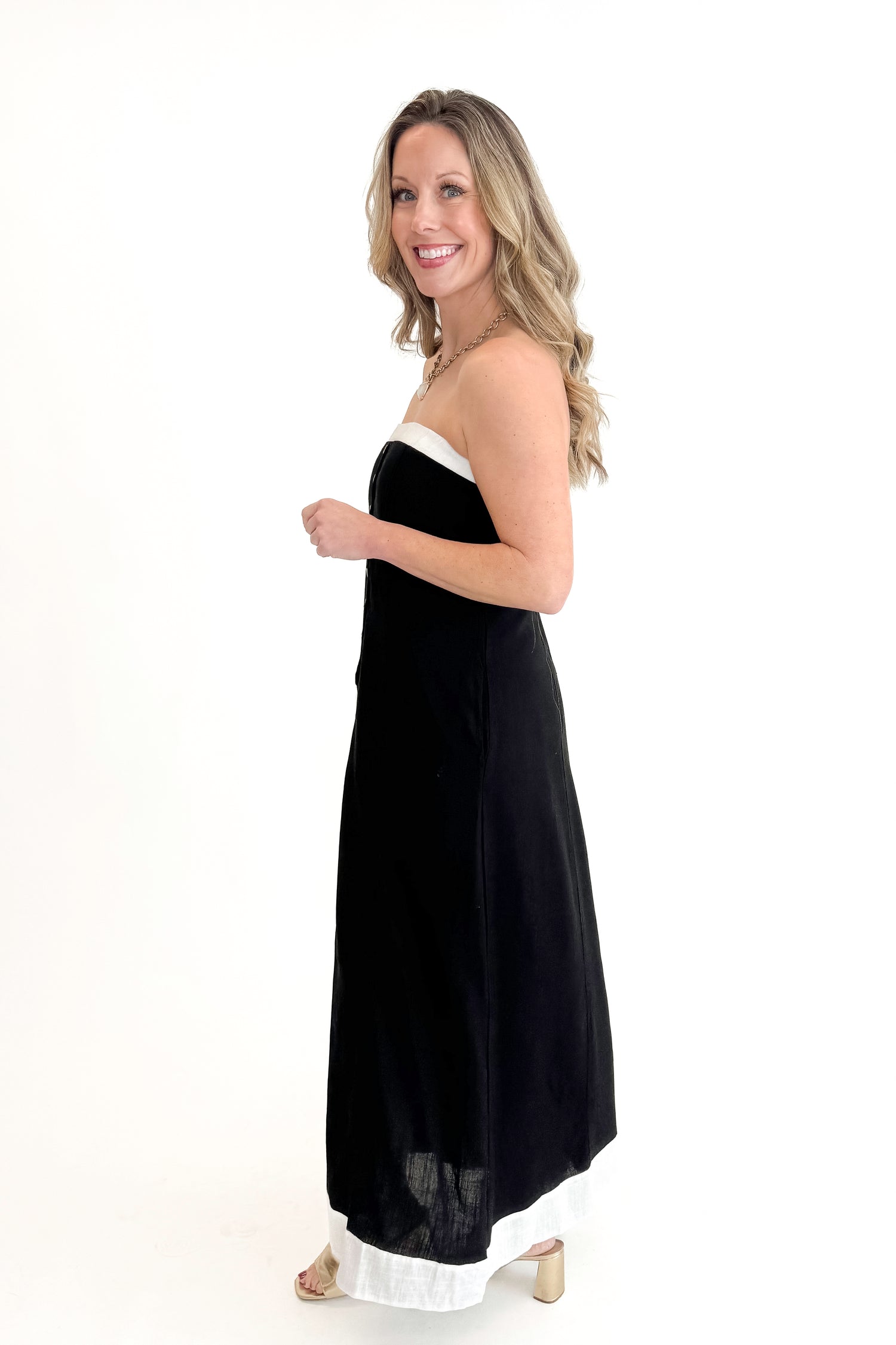 Side view of woman wearing Black With White Lining Button Down Strapless Dress against white studio background.