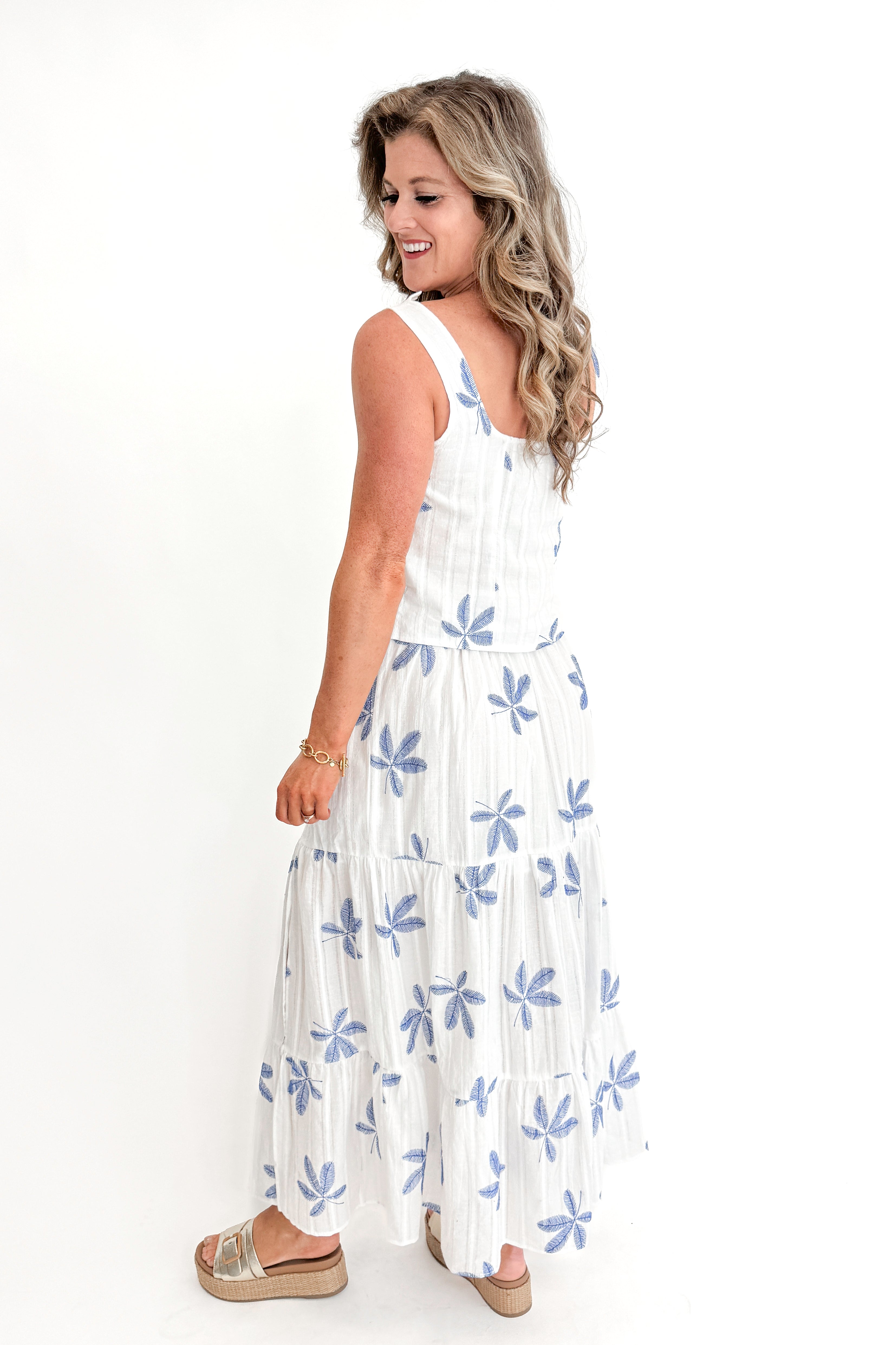Side view of woman wearing White With Blue Embroidery Top with matching skirt against white studio background.