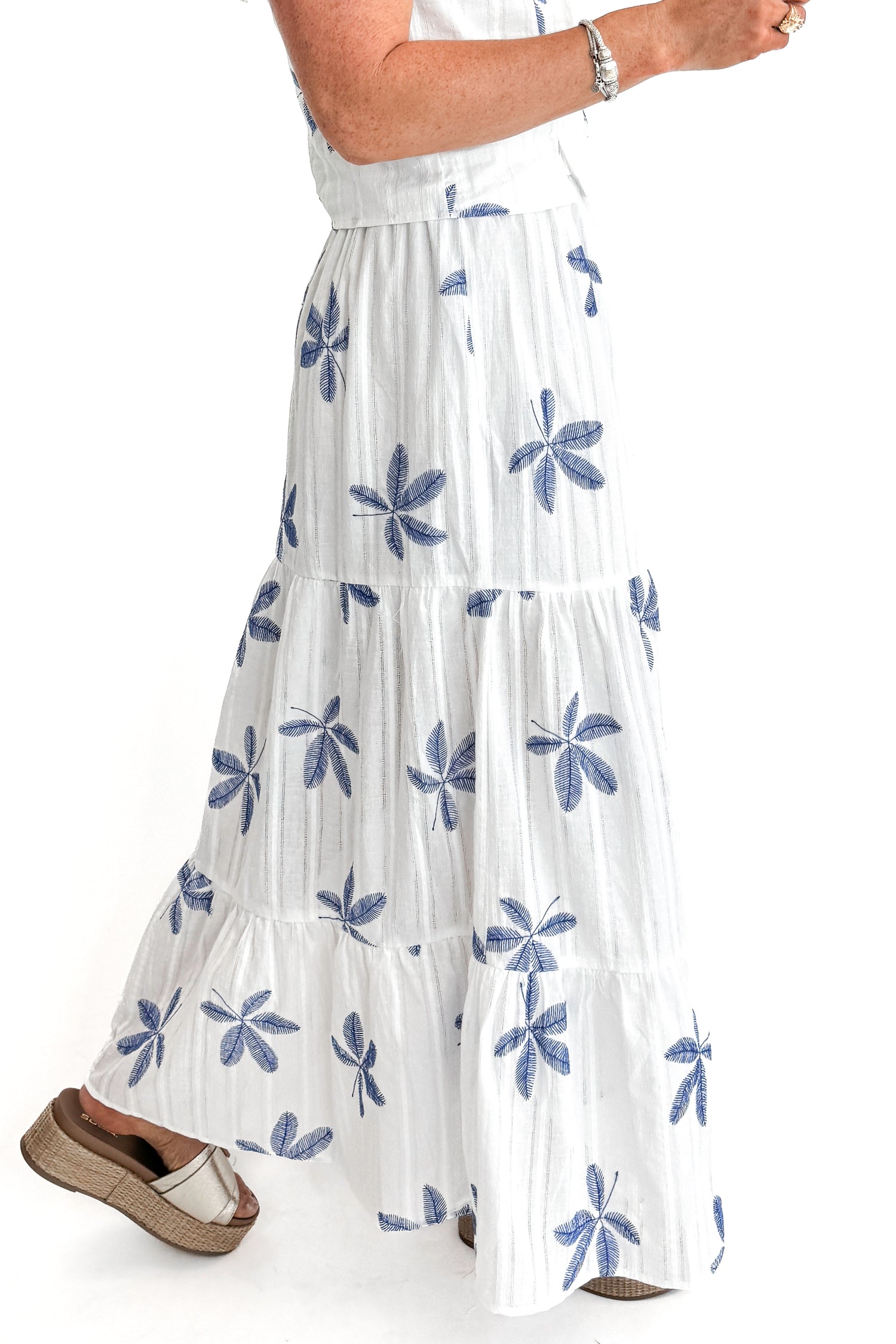 Side view of woman wearing White With Blue Embroidery Tiered Skirt with matching top against white studio background.