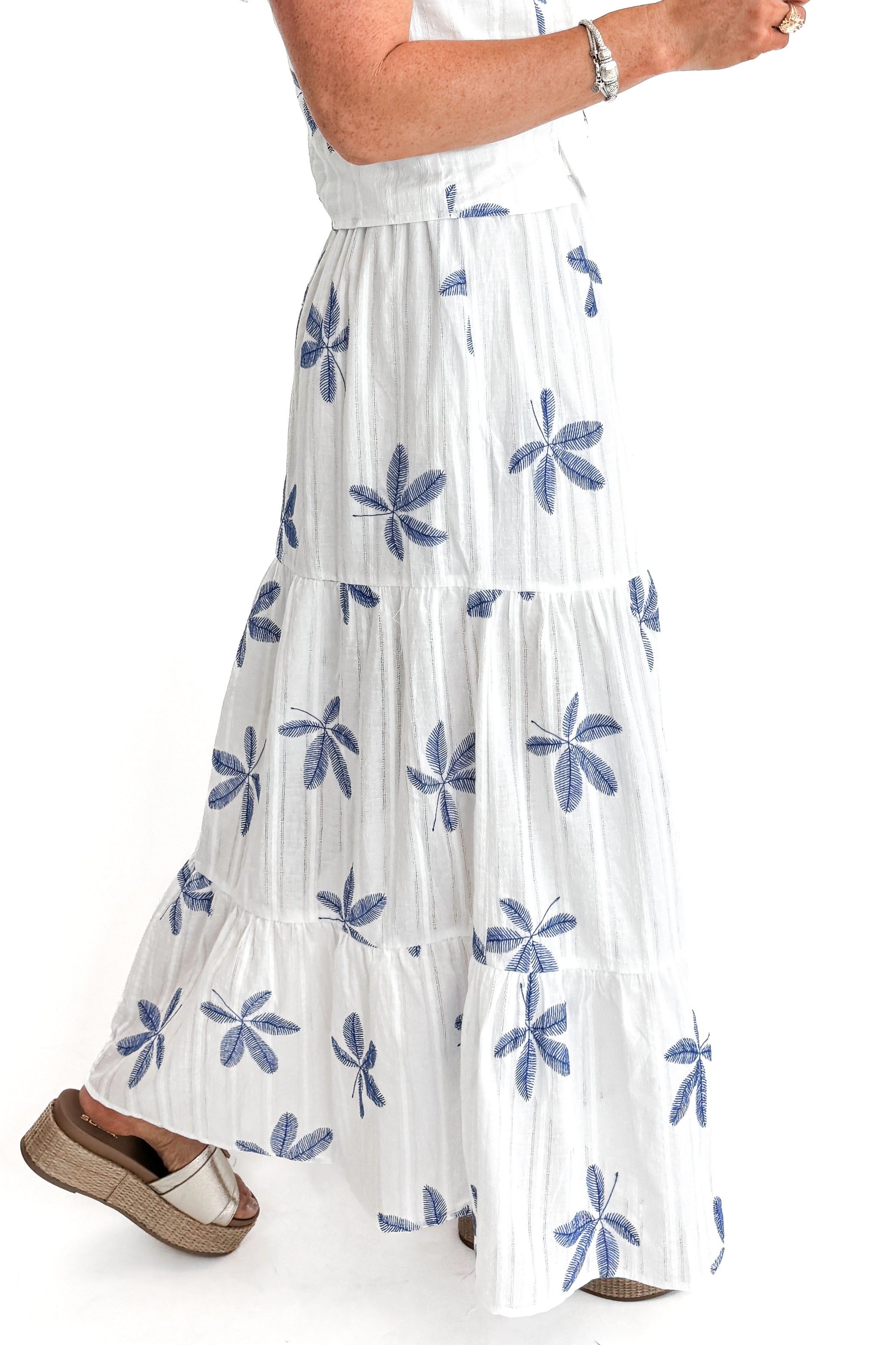 Side view of woman wearing White With Blue Embroidery Tiered Skirt with matching top against white studio background.