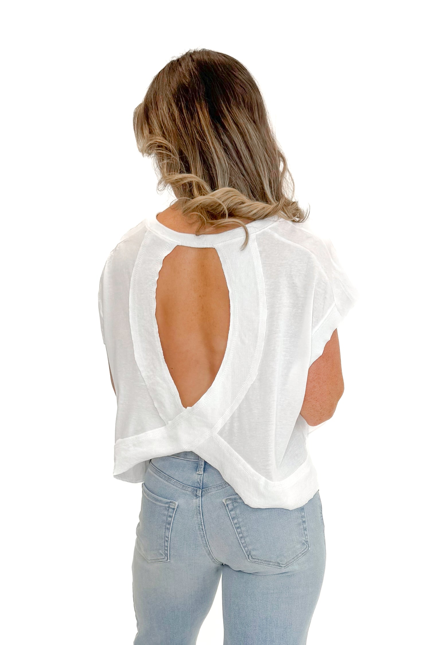 Back view of woman wearing White Cut Out Back Tee with jeans against white studio background.