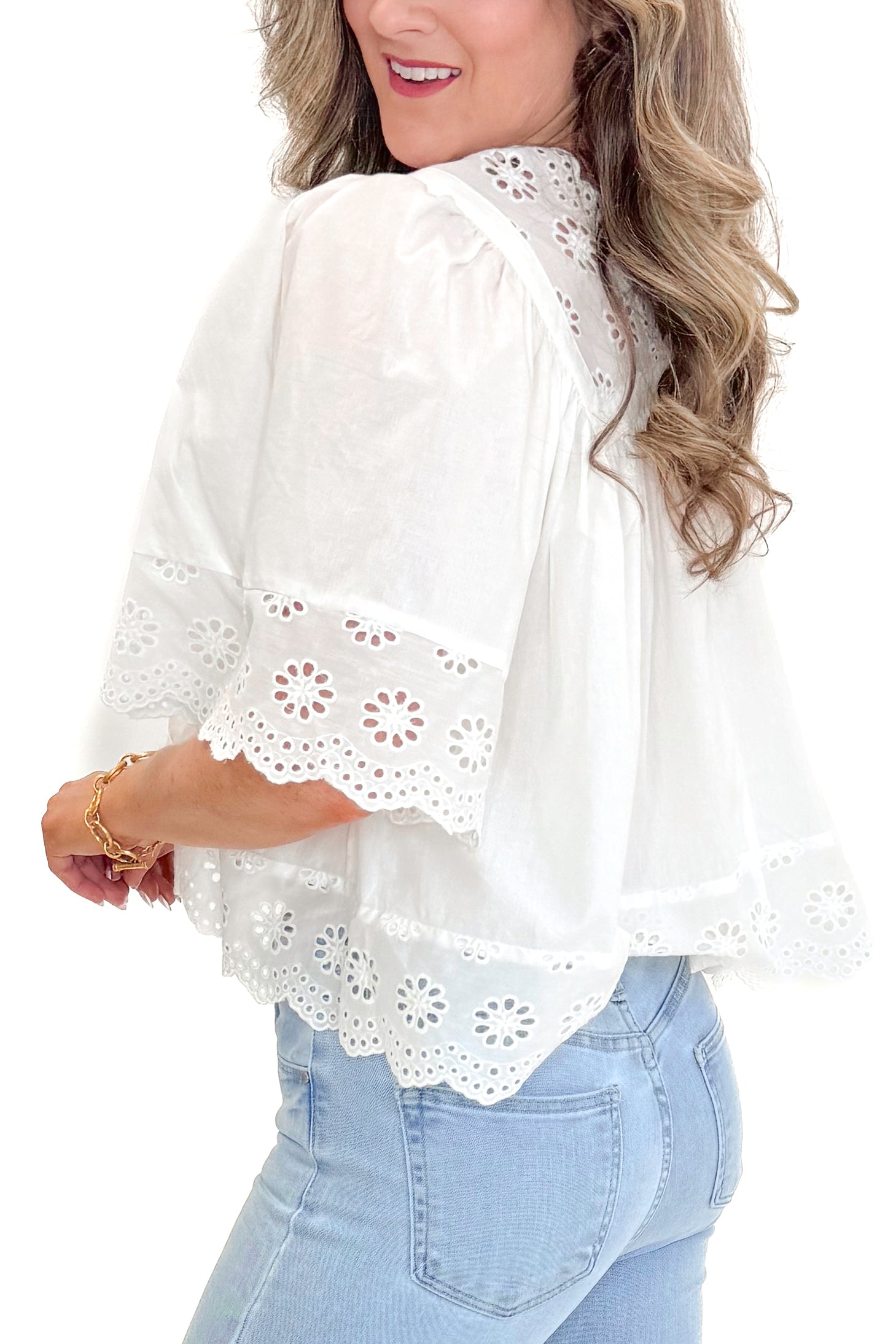 Side view of woman wearing White Eyelet Babydoll Top with jeans against white studio background.