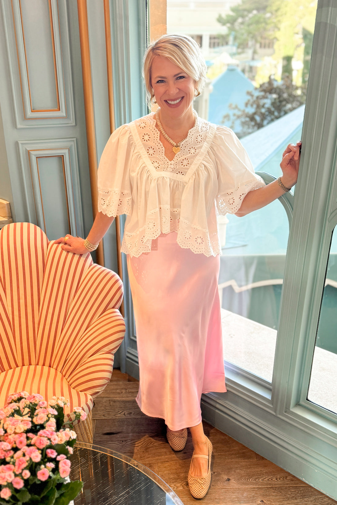 Front view of woman wearing Soft Pink Satin Skirt with White Eyelet Babydoll Top at a restaurant.