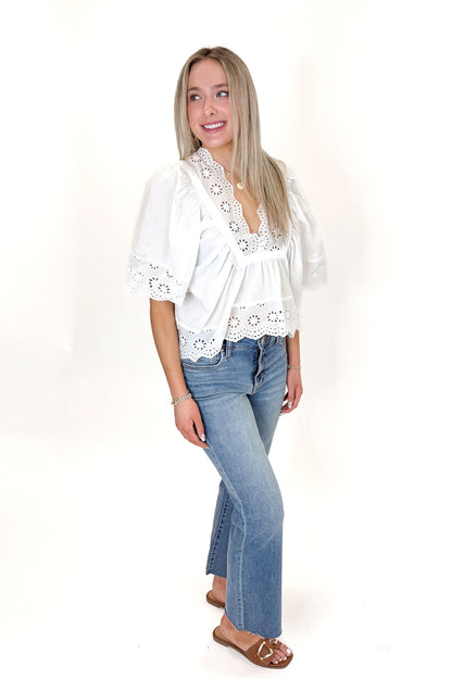 Side view of woman wearing White Eyelet Babydoll Top with jeans against white studio background.