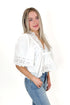 Side view of woman wearing White Eyelet Babydoll Top with jeans against white studio background.