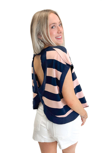Side view of woman wearing Navy &amp; Pink Striped Cut Out Back Tee with jean shorts against white studio background.