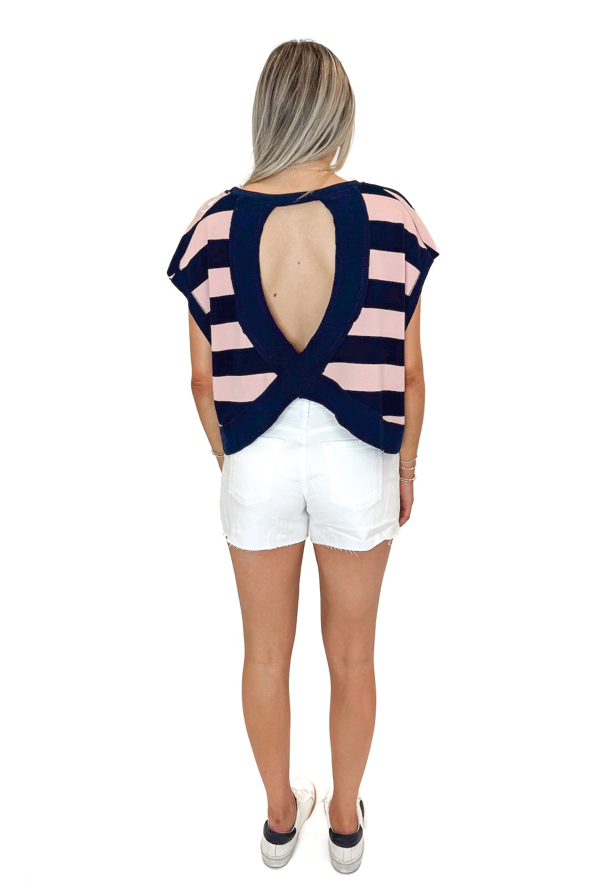 Back view of woman wearing Navy &amp; Pink Striped Cut Out Back Tee with jean shorts against white studio background.