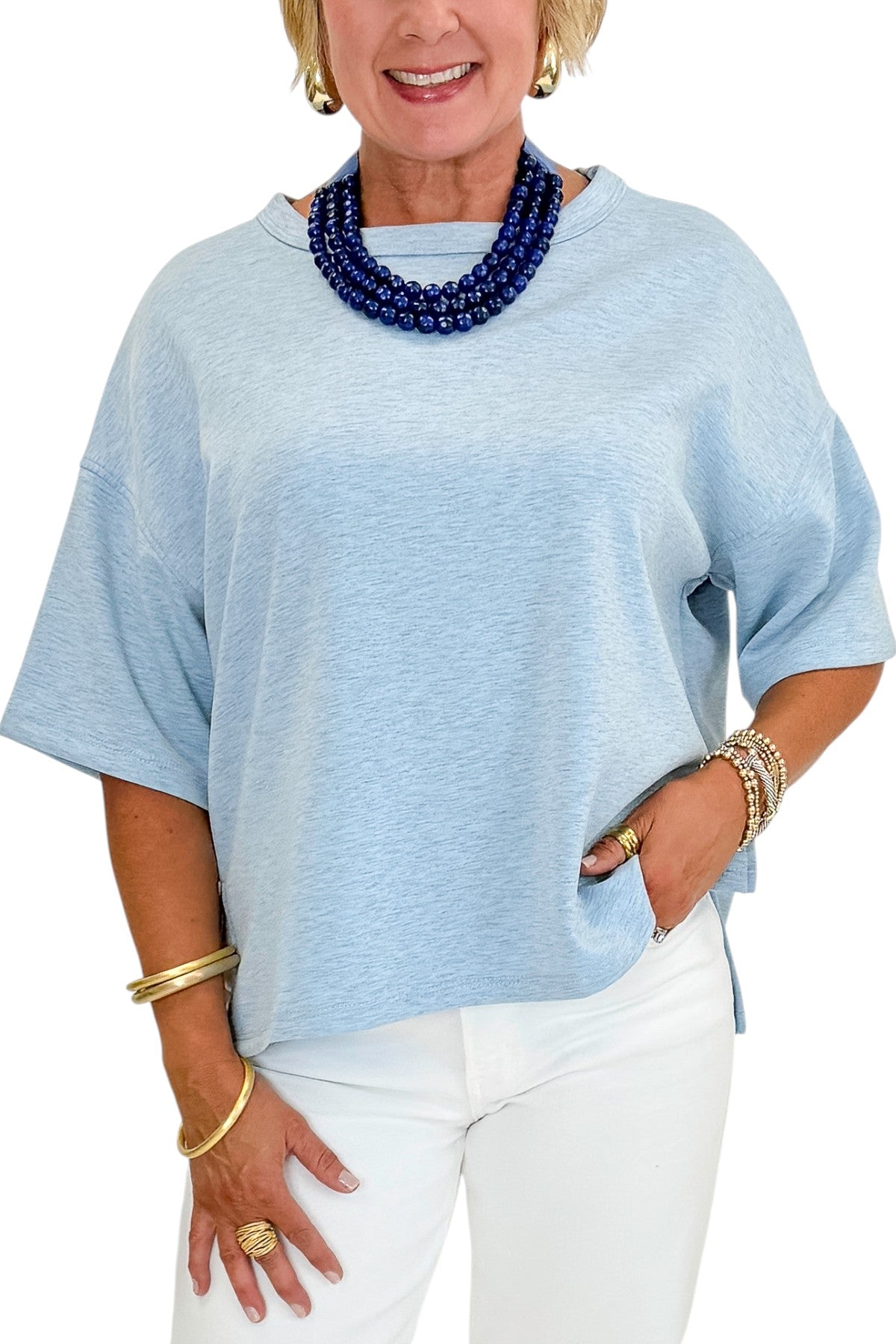 Front detail view of woman wearing Swagger Boutique’s Heathered Blue Short Sleeve Top with jeans against white studio background.