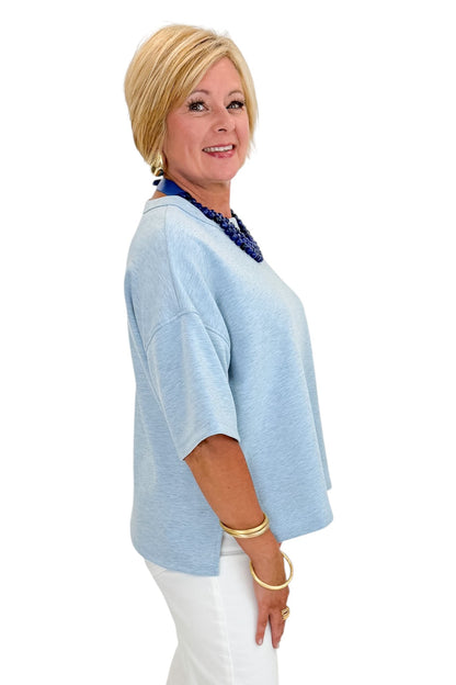 Side view of woman wearing Swagger Boutique’s Heathered Blue Short Sleeve Top with jeans against white studio background.