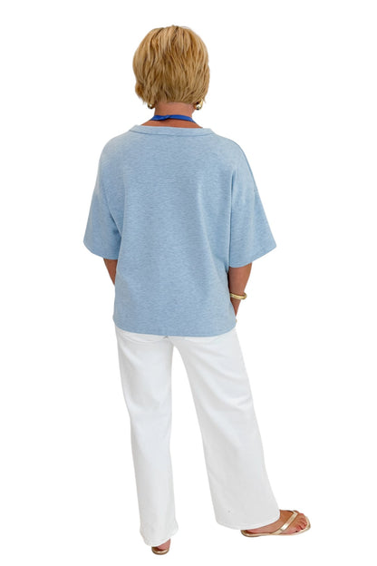 Back view of woman wearing Swagger Boutique’s Heathered Blue Short Sleeve Top with jeans against white studio background.