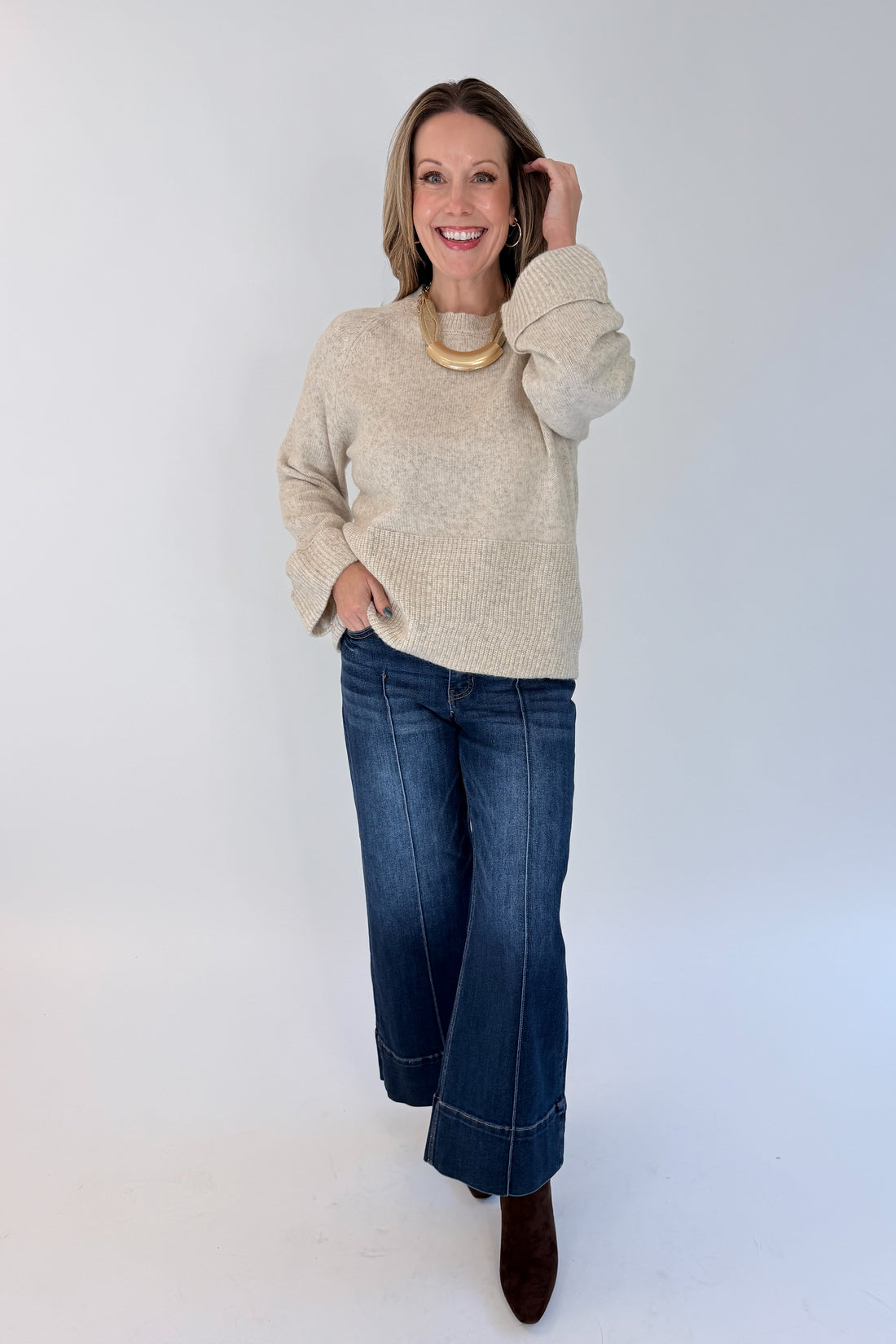 Front view of woman wearing Swagger Boutique’s Heathered Oatmeal Cuffed Sleeve Sweater with jeans against white studio background.
