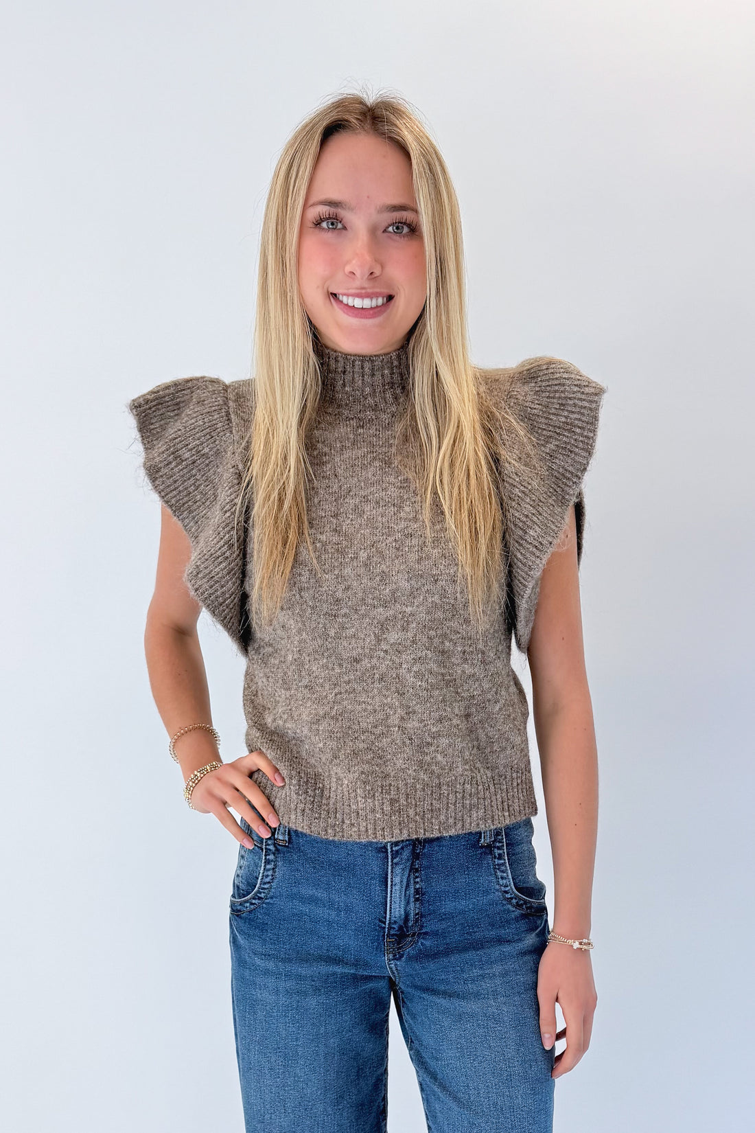 Front view of woman wearing Swagger Boutique’s Heathered Taupe Short Flutter Sleeve Sweater by Entro with jeans against white studio background.