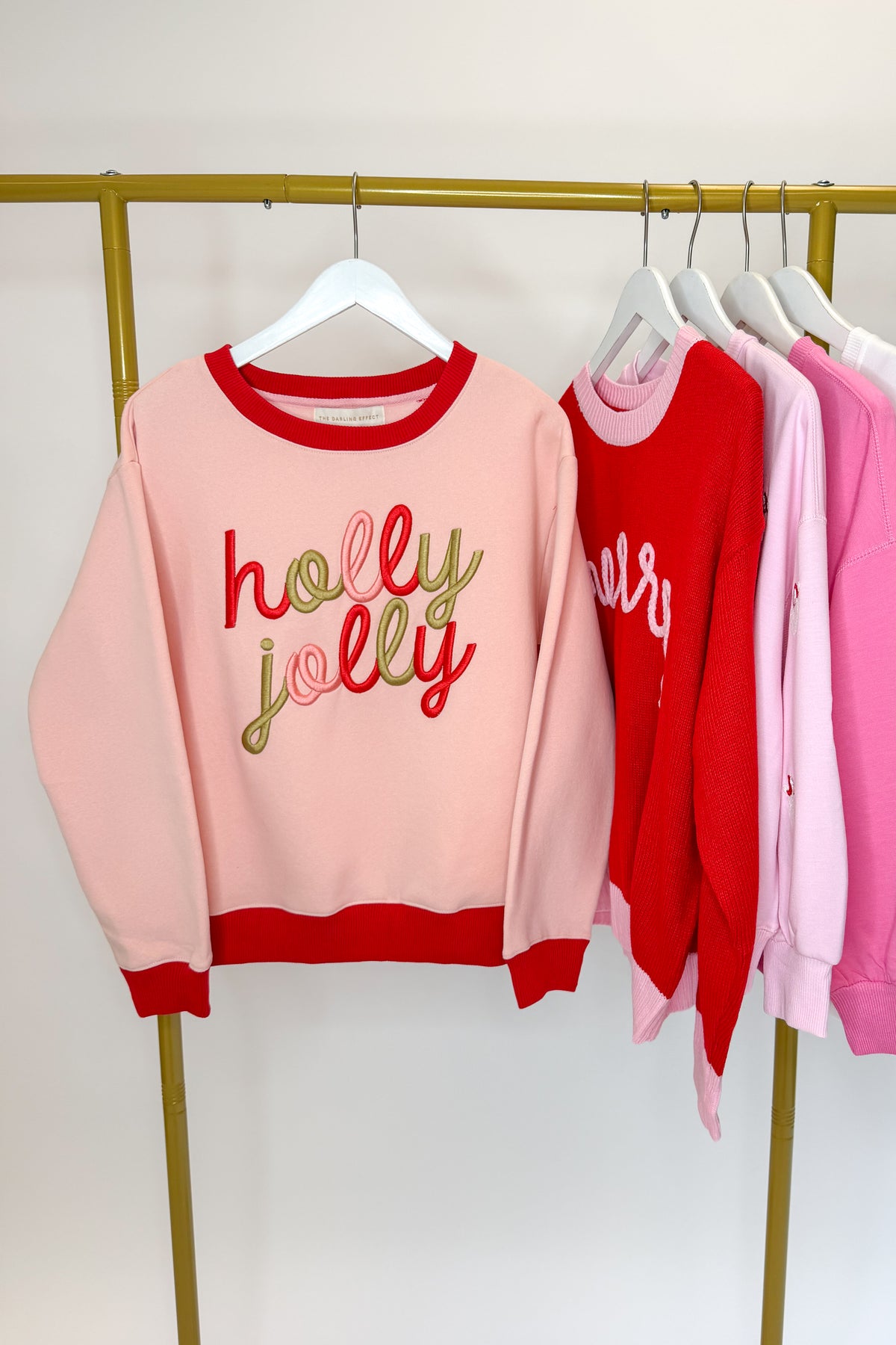 Swagger Boutique’s Holly Jolly Signature Crew Sweatshirt hanging on a rack with other holiday sweatshirts. 